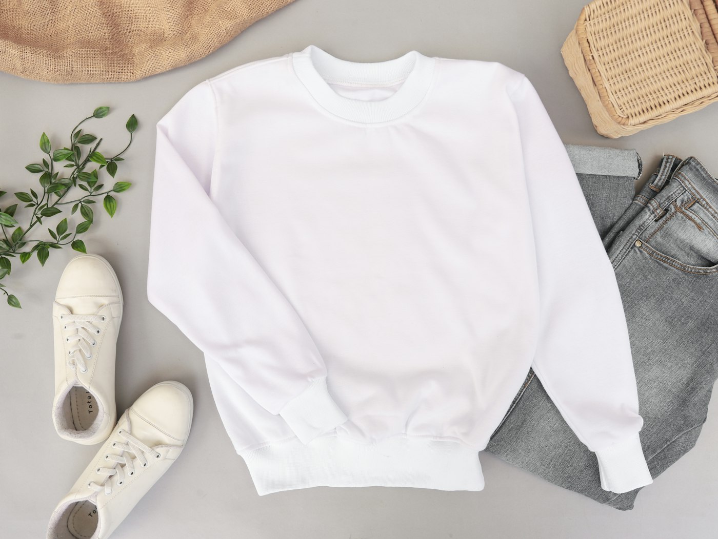 Weißer Pullover flach gelegt neben Jeans und Schuhen